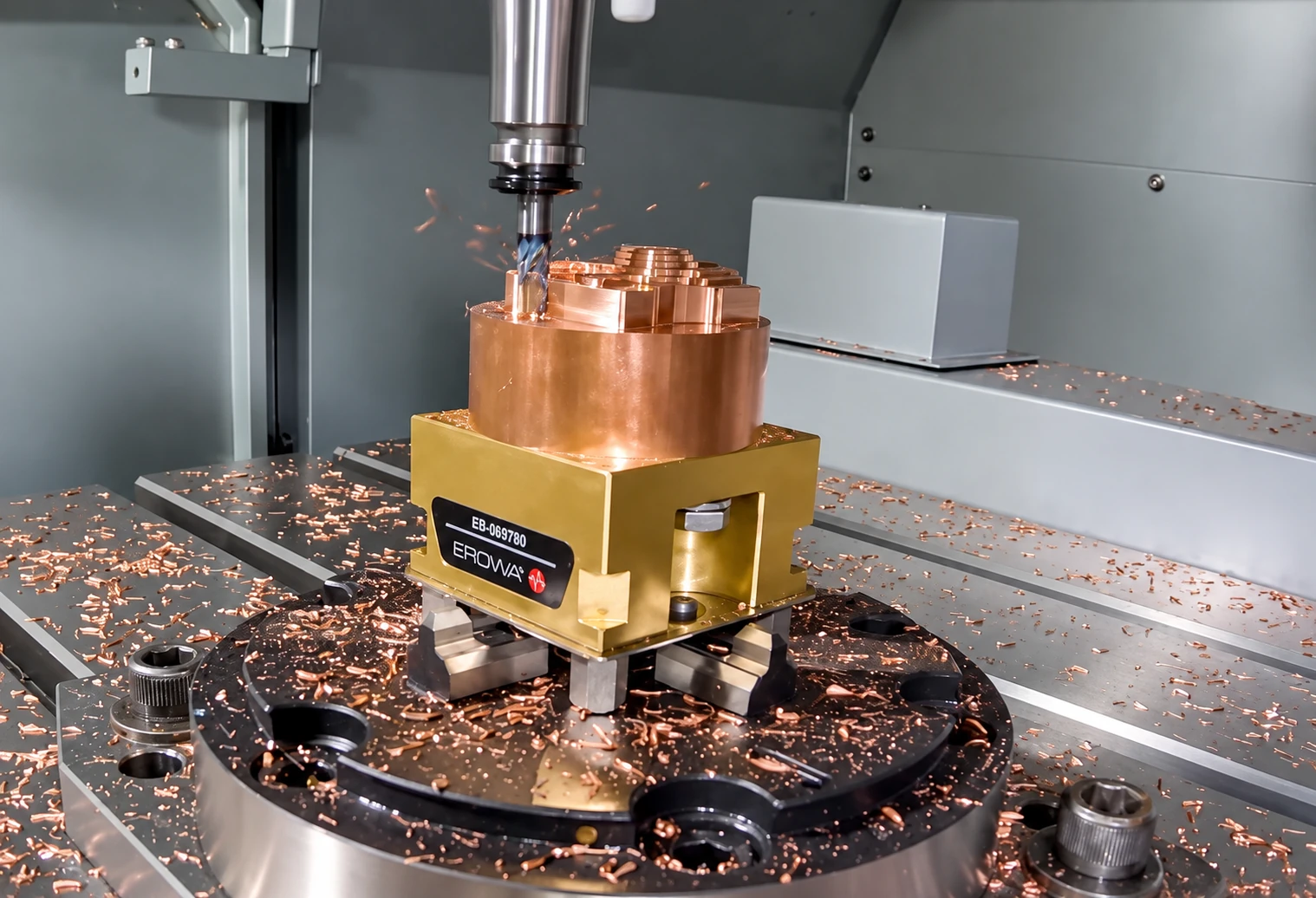 Milling tool above a stepped copper-colored workpiece held in a fixture inside a machining center.