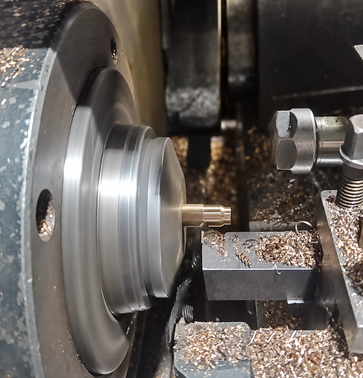 Lathe tool beside a small stepped workpiece projecting from a rotating chuck.