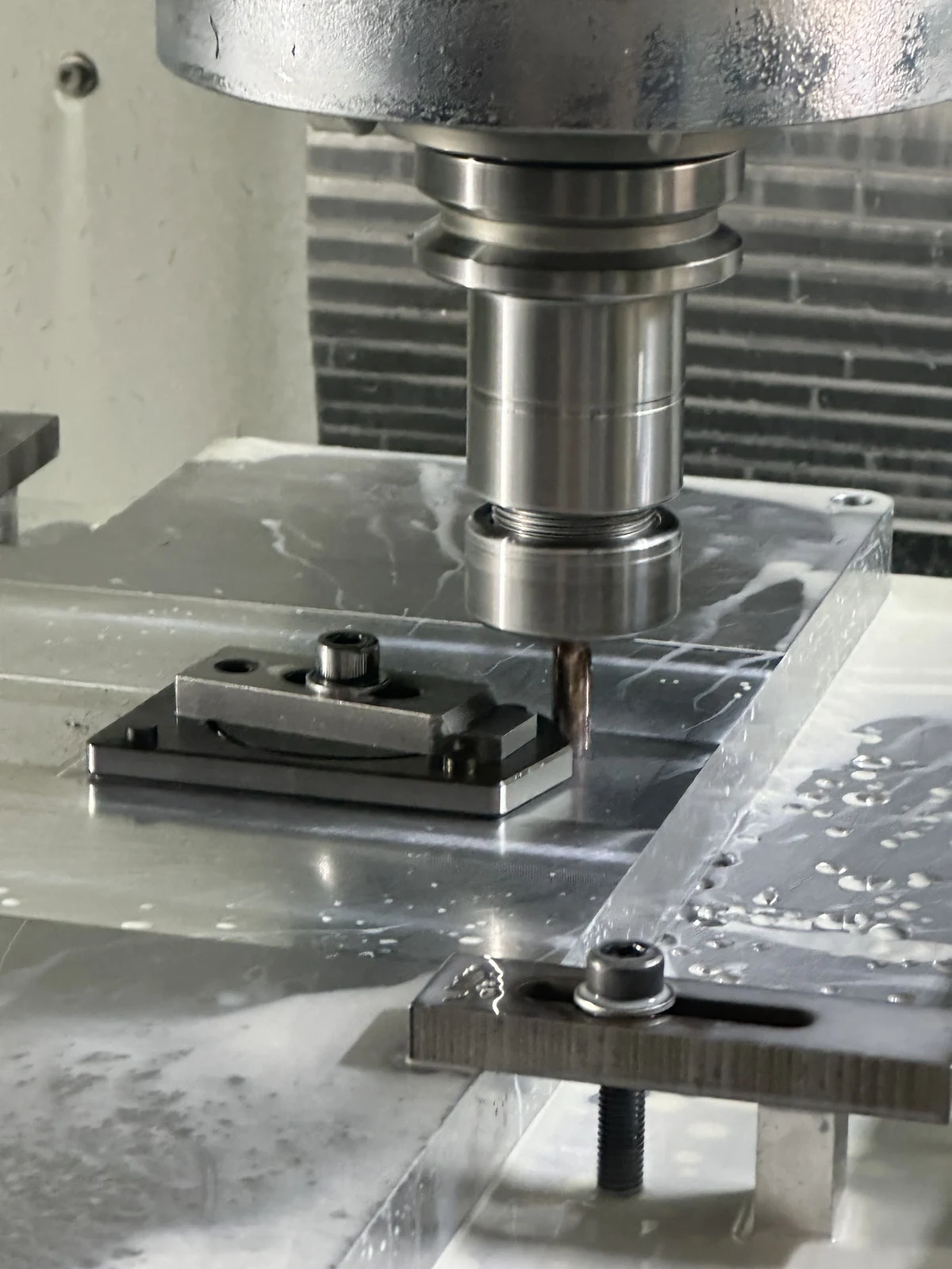 End mill held in a vertical spindle beside a clamped workpiece on a CNC machine table.